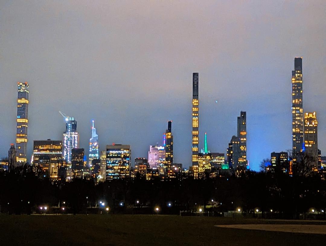 An image of Midtown Manhattan from Central Park with Times Square glowing from its lights