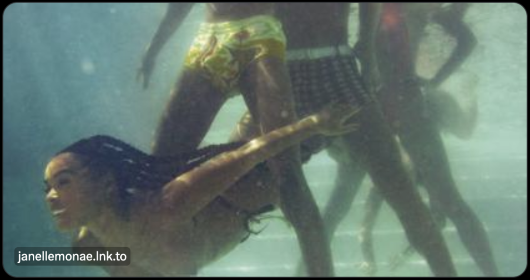 Album cover of the The Age of Pleasure byt Janelle Monae. Shows an underwater scene of a three men standing in a pool while a women swims underwater and between their legs.